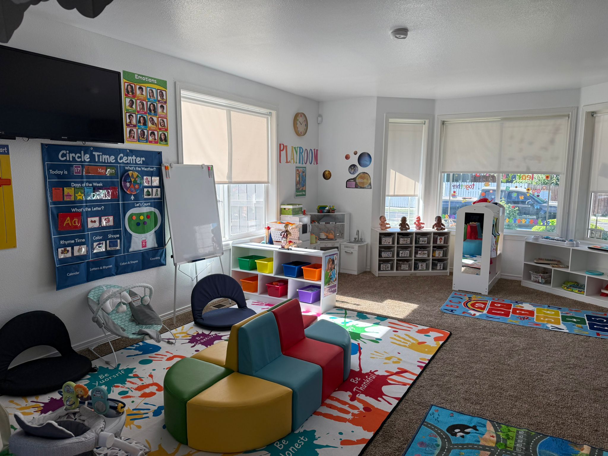 Aula de preescolar luminosa y organizada con muebles de colores, carteles educativos, contenedores, una pizarra y juguetes ordenados en estantes.